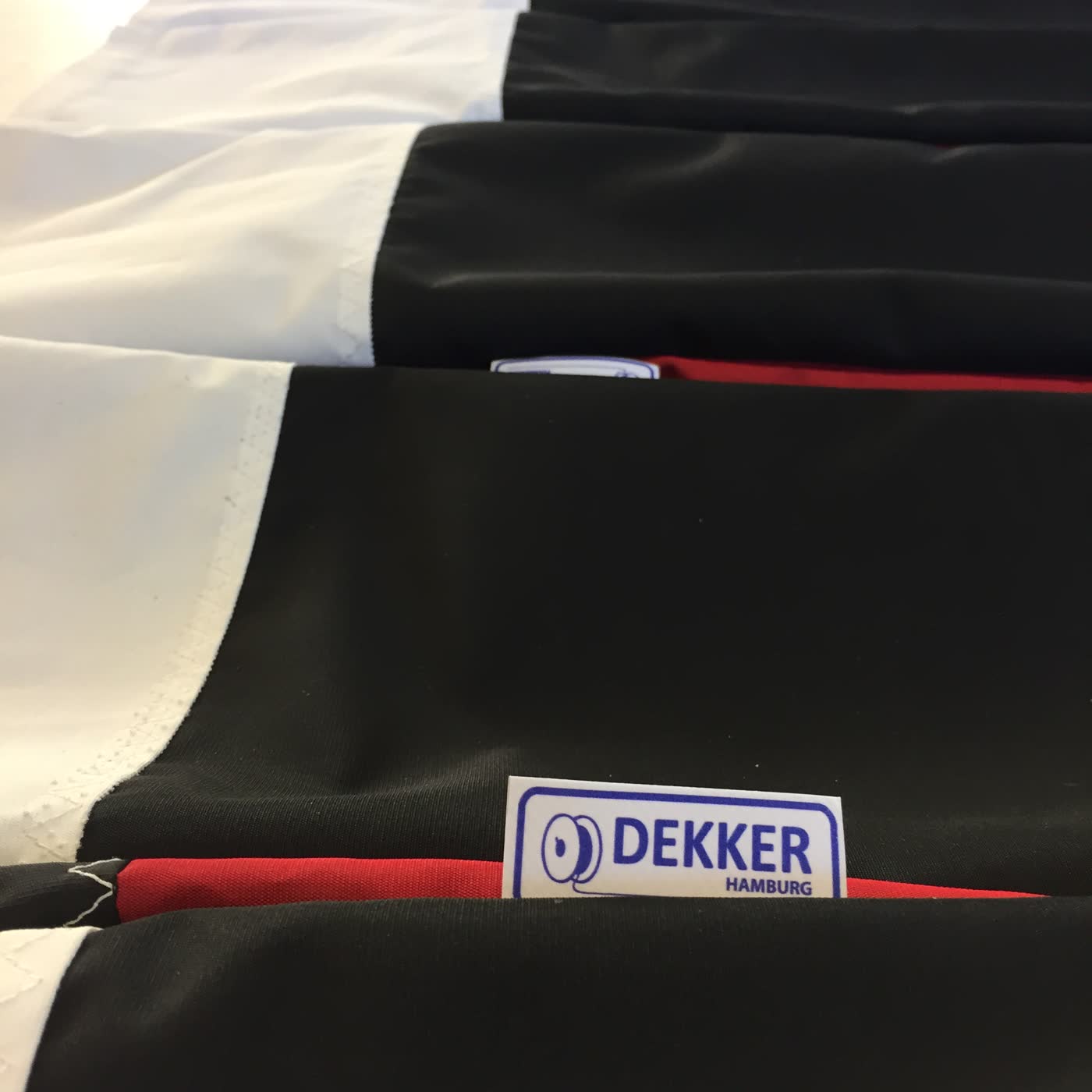 Reihe gleicher Polsterbezüge in Schwarz, Rot und Weiß mit Dekker Hamburg Etikett